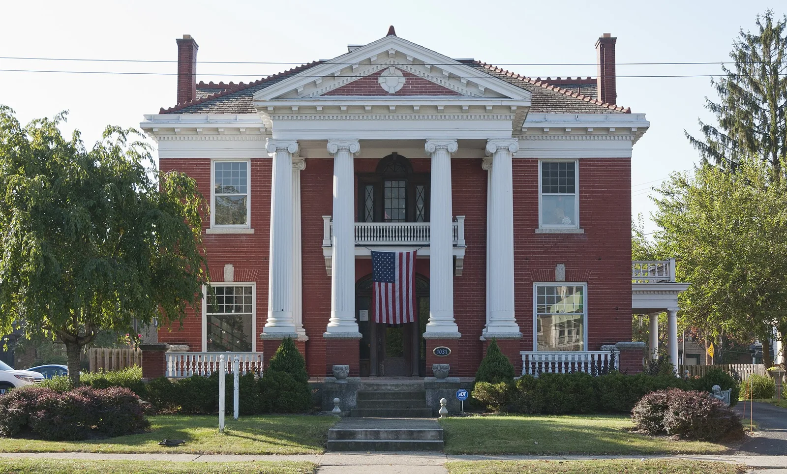Red brick house with a white columned porch and mature trees
