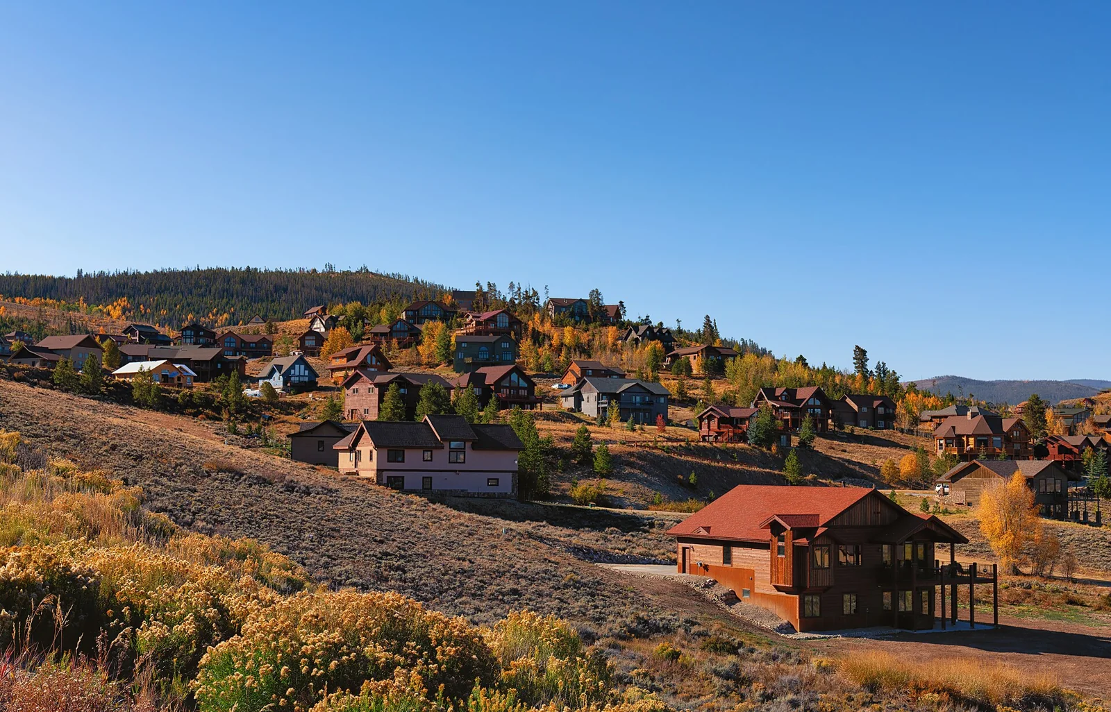 Distinct homes spread across a golden hillside below a clear blue sky